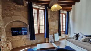 A cozy living room with a stone wall, a flat-screen TV mounted on the wall, a wooden ceiling, and a sofa with cushions. - 
Chic Studio in Old Bergerac (Bergerac)