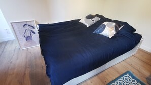 A bed with a dark blue bedspread and patterned pillows, a framed artwork on the wall, and a wooden floor. - 
Chic Studio in Old Bergerac (Bergerac)
