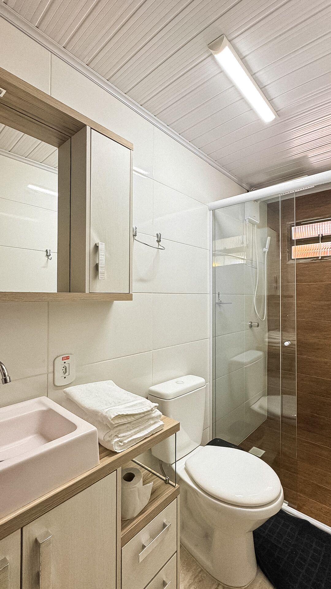 Un baño moderno con lavamanos, espejo, inodoro y ducha.