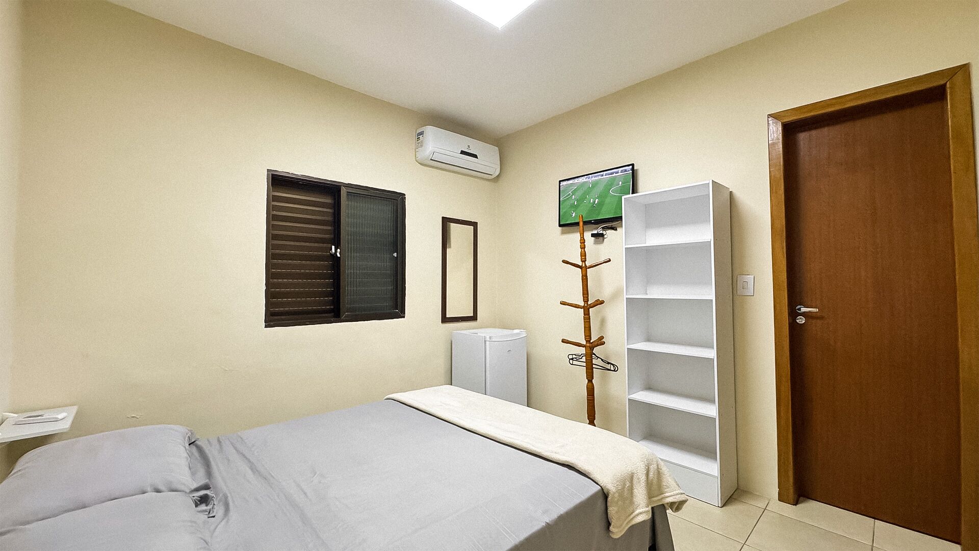Quarto com cama, guarda-roupa, radiador, espelho e porta.