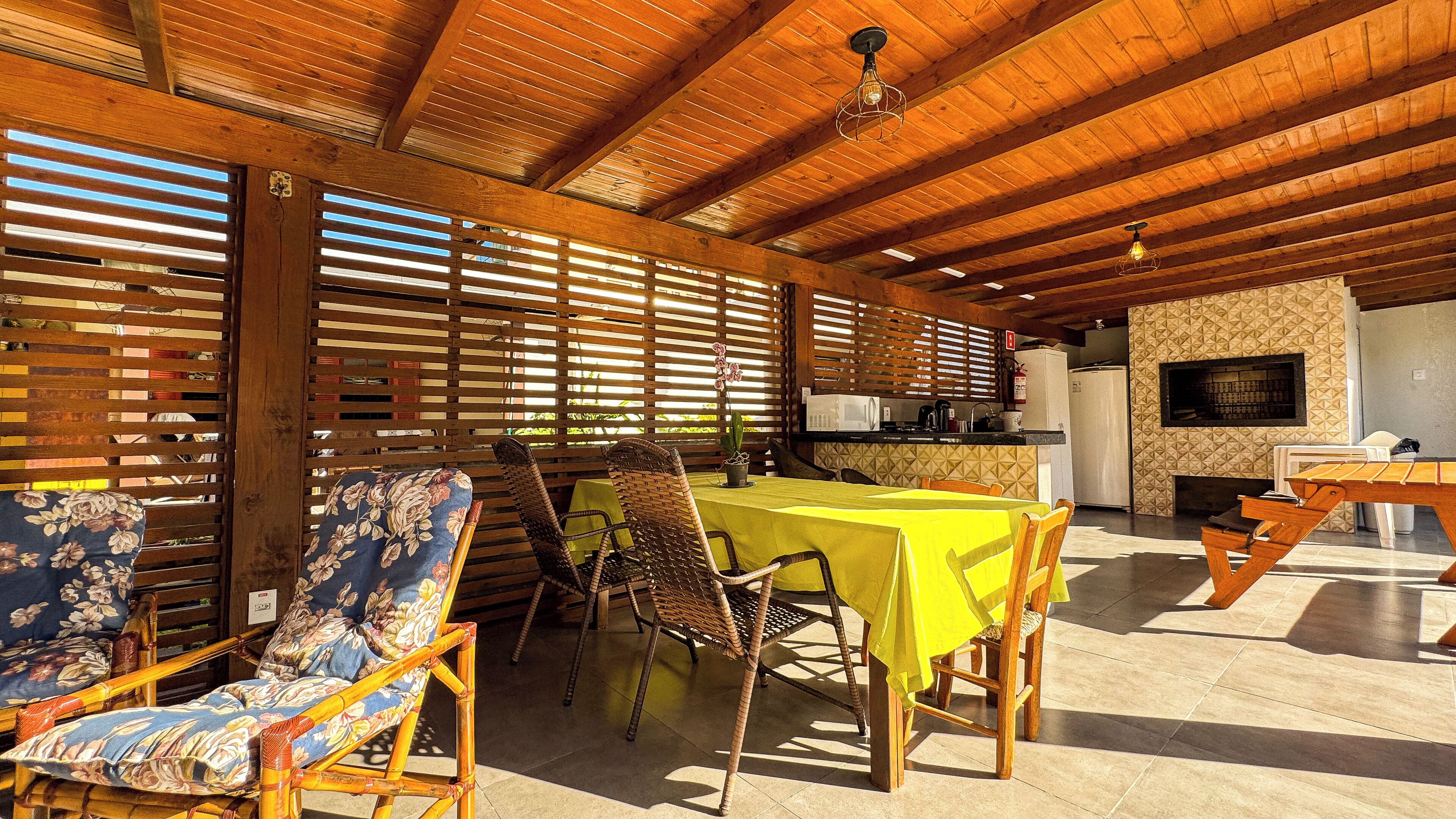 Un área de comedor al aire libre techada, con mobiliario de madera y una cocina al fondo.