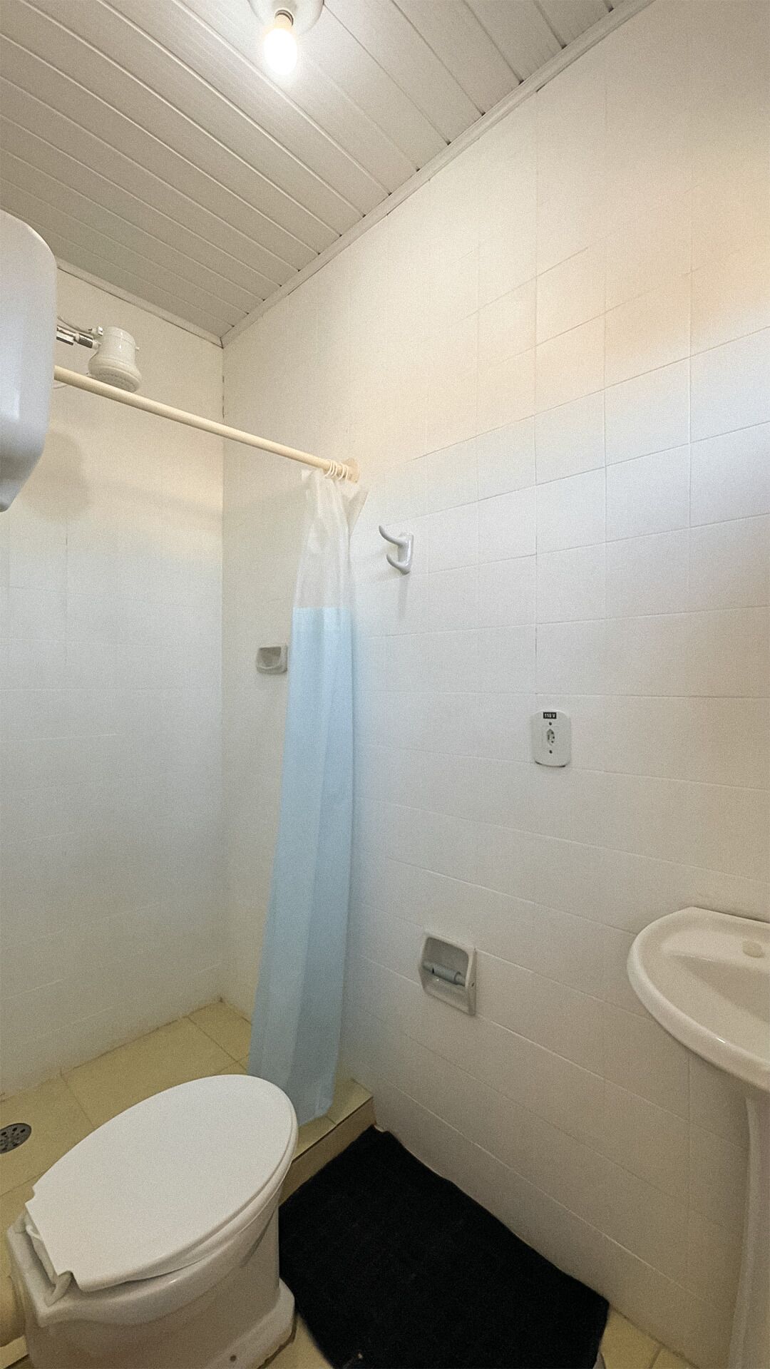 Un baño pequeño con inodoro, cortina de ducha, lavamanos e iluminación en el techo.