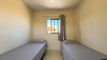 A small, single-room accommodation with two single beds, a window with curtains, and a view of buildings outside.