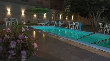 A swimming pool with lounge chairs and tables, surrounded by walls with built-in lighting.