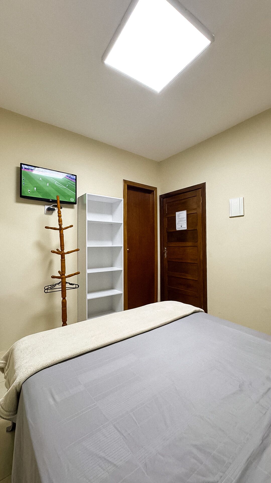 A bedroom with a bed, a television mounted on the wall, a coat rack, a wardrobe, and a door.