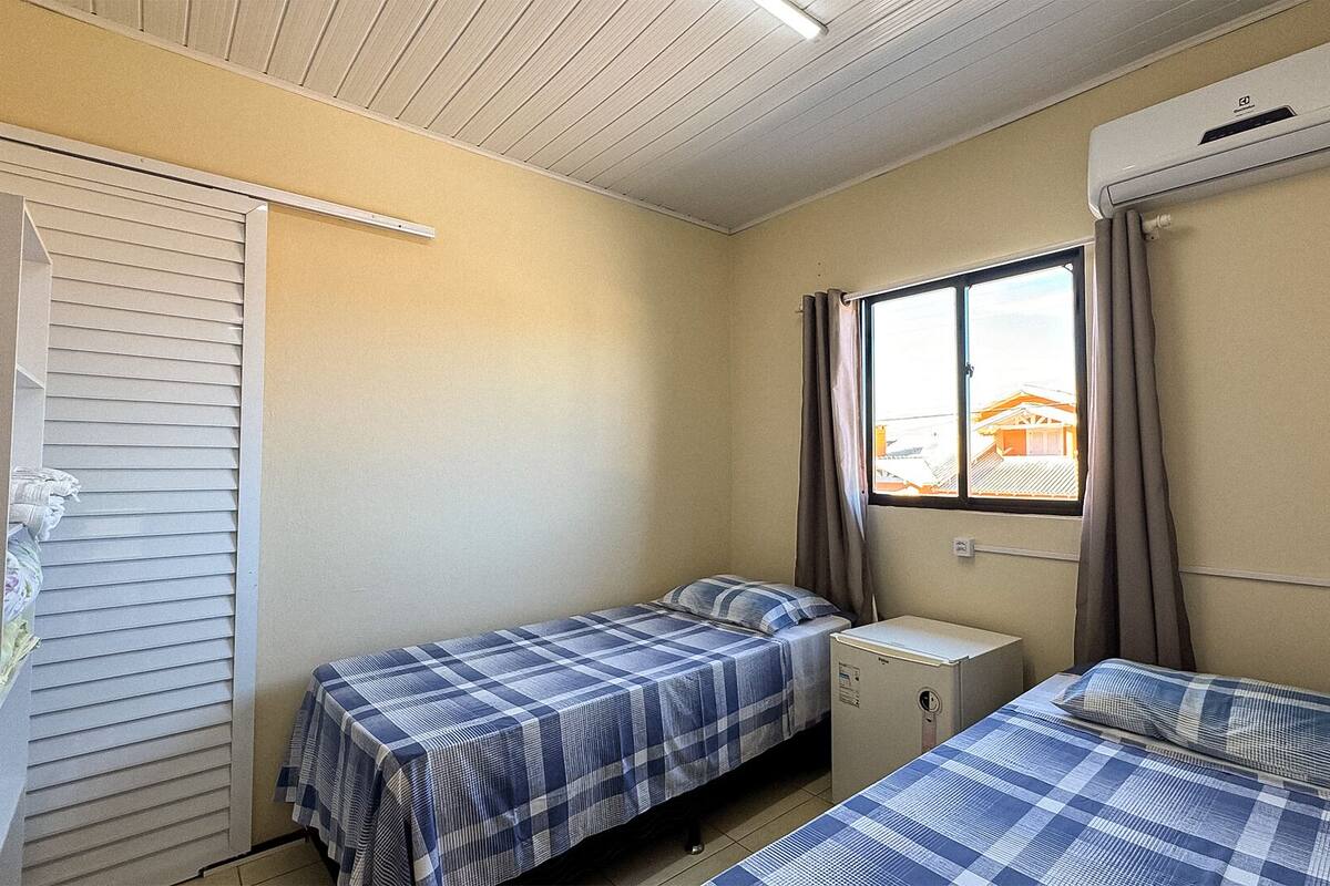 Pieni, yhden huoneen asunto, jossa on kaksi sänkyä, ikkuna verhoilla ja ilmastointilaite.