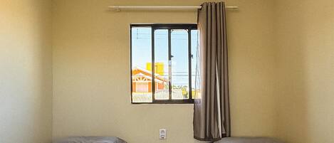 A small, single-room hotel room with two beds, a window with curtains, and a tiled floor.