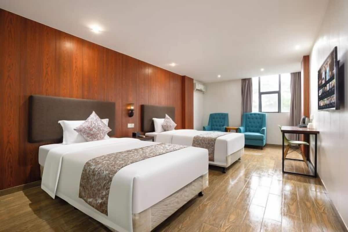 Habitación de hotel con dos camas, un sillón azul, una mesita y un televisor en la pared.