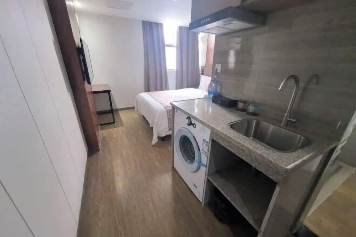 Una habitación de hotel compacta con kitchenette, lavadora, cama y una pequeña mesa.
