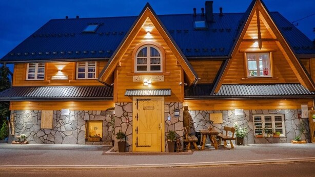 A wooden lodge with a stone facade, a central entrance, and a dining area with outdoor seating.