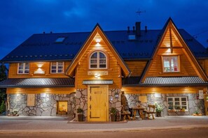 A wooden lodge with a stone facade, a central entrance, and a dining area with outdoor seating. - Willa Mnich (Bukowina Tatrzanska)
