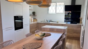 A modern kitchen with white cabinets, a wooden dining table, and pendant lights.