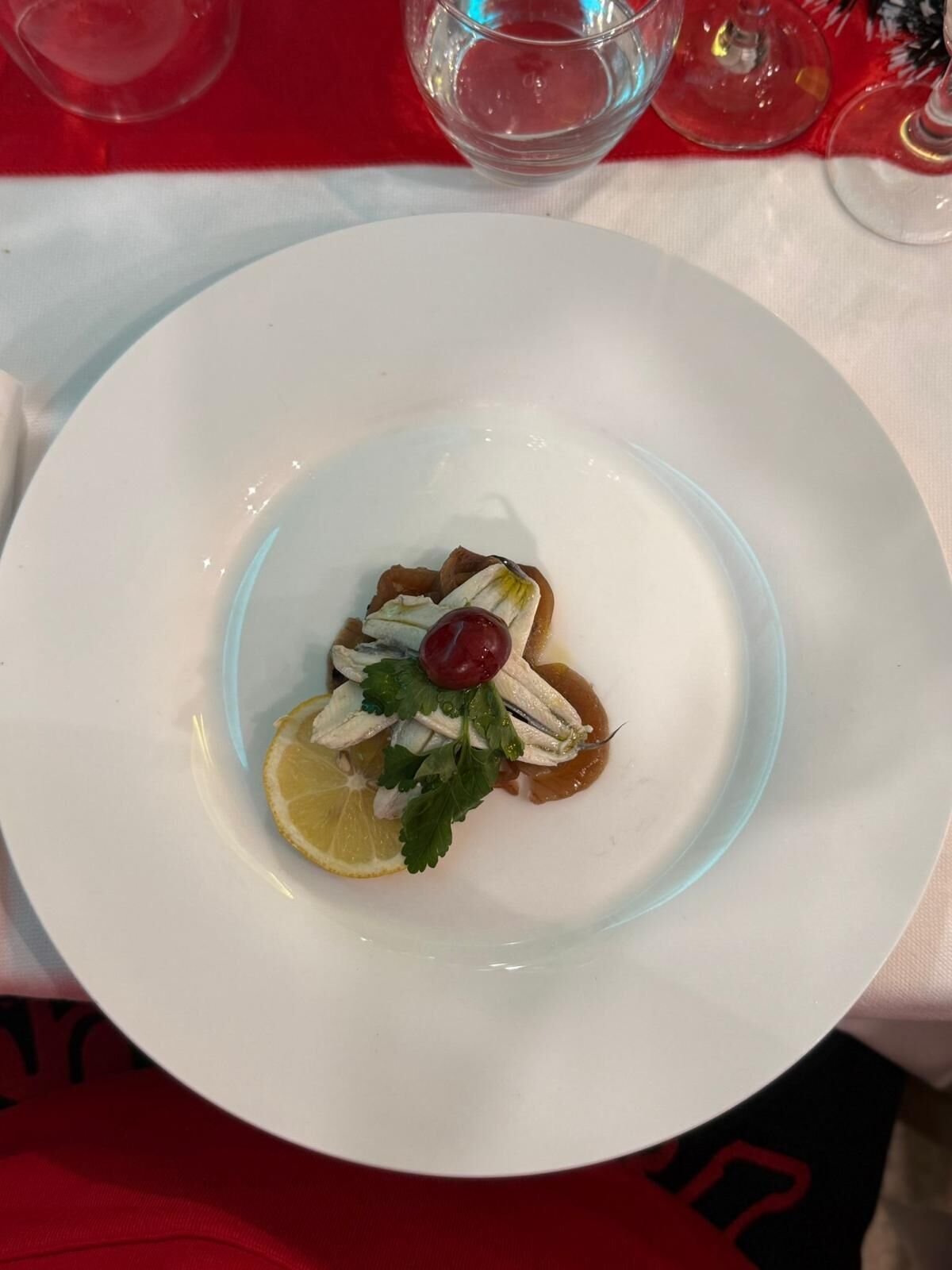 A white plate with a seafood dish, garnished with lemon and parsley, on a table with a red tablecloth.