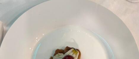 A white plate with a seafood dish, garnished with lemon and parsley, on a table with a red tablecloth.