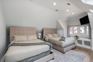 Quarto com duas camas, uma mesa de cabeceira, uma janela com cortinas e um banco embutido.