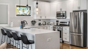 A modern kitchen with white cabinets, stainless steel appliances, a large island with bar stools, and pendant lighting.