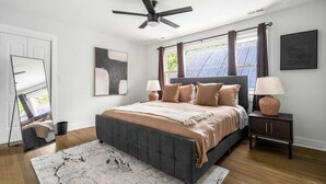 A bedroom with a bed, a ceiling fan, a nightstand, a lamp, and a large window with curtains.