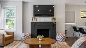 A modern living room with a fireplace, a flat-screen TV mounted above it, and a dining area with a bar.