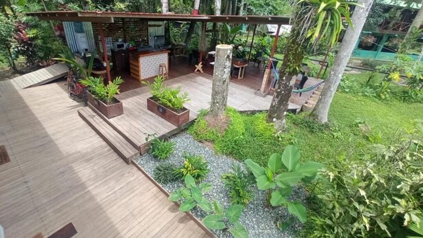 Una terraza de madera con zona de estar, rodeada de exuberante vegetación y un pequeño jardín.