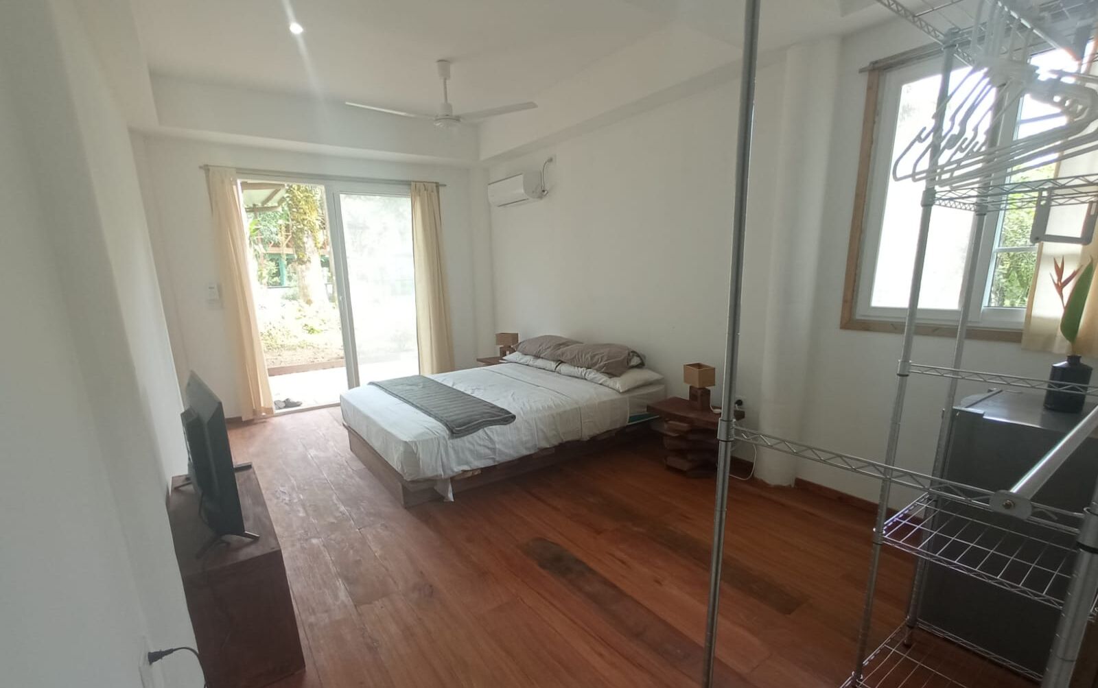 Une chambre à coucher avec un lit, un ventilateur de plafond, une fenêtre et un étagère en métal.