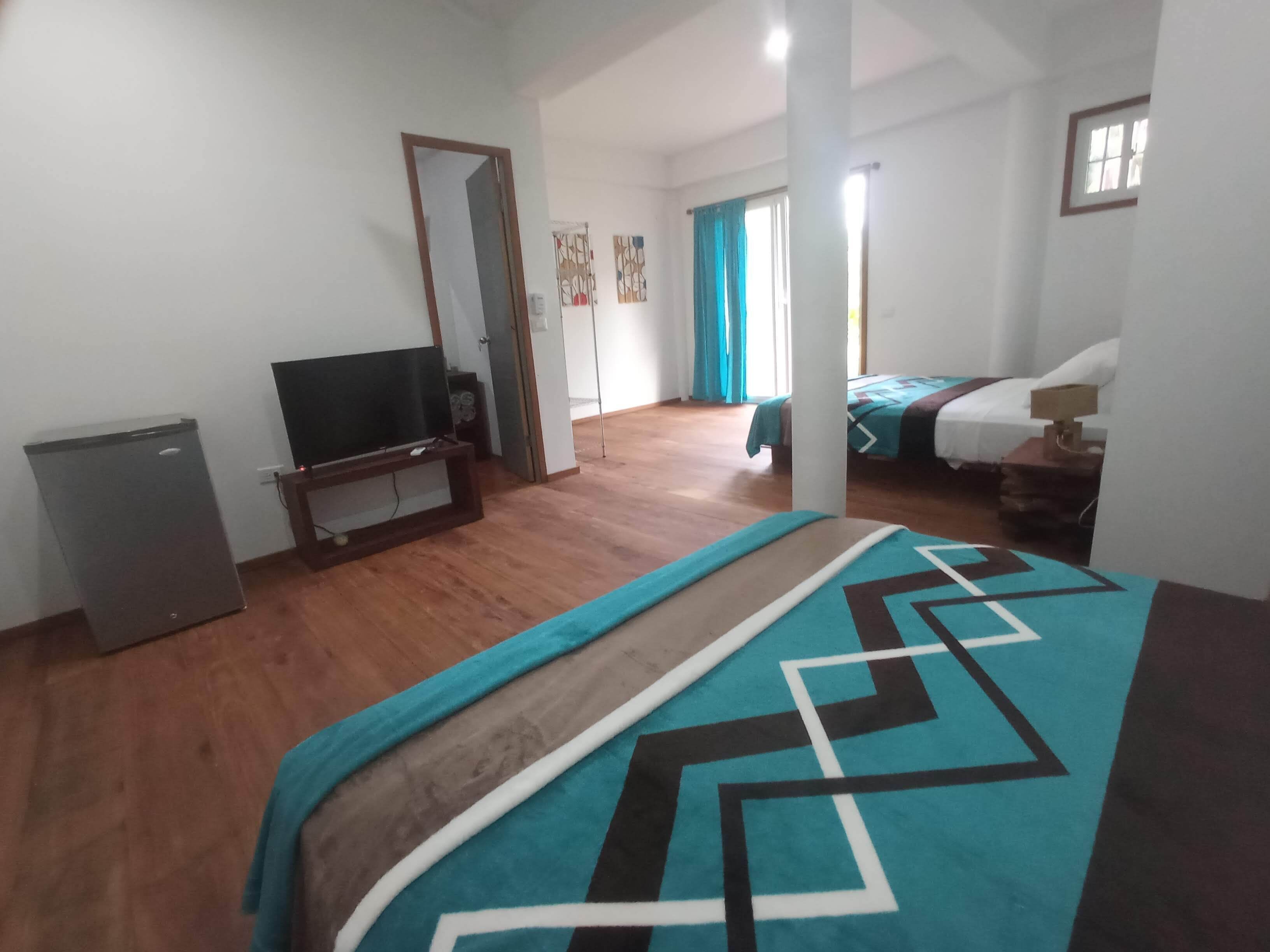 Une chambre d’hôtel avec un lit, une télévision, un petit réfrigérateur et une salle de bain que l’on aperçoit à l’arrière-plan.
