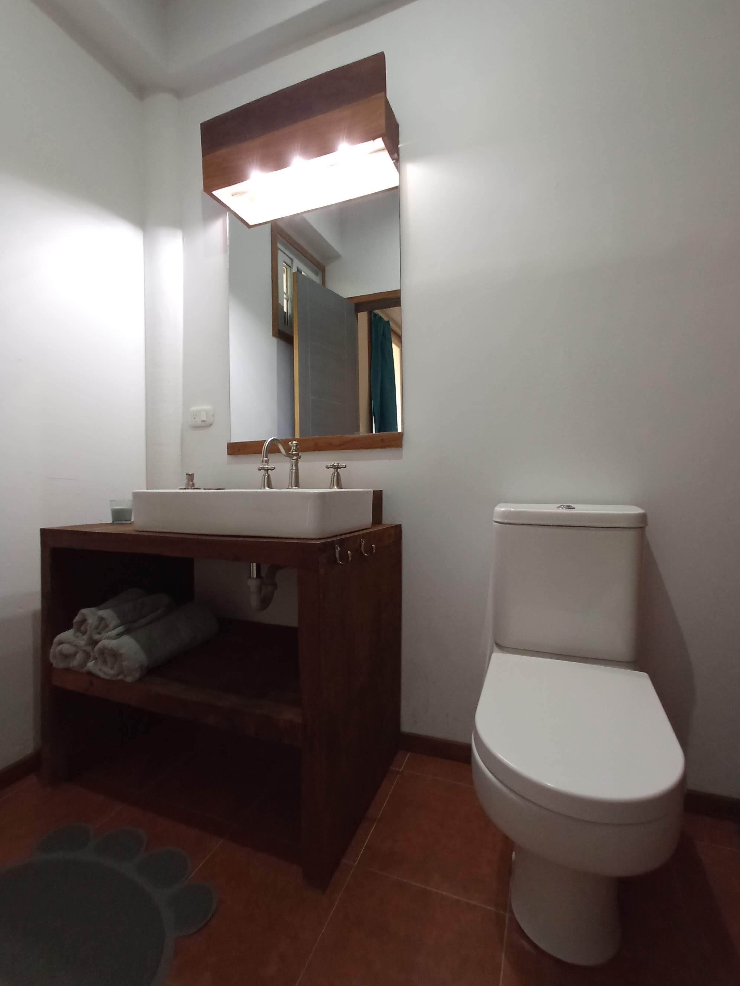 Un baño con un lavabo blanco, un espejo encima, un inodoro y un perchero con toallas.