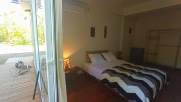A bedroom with a bed, a wooden floor, a nightstand, a lamp, and a view of the outdoors.