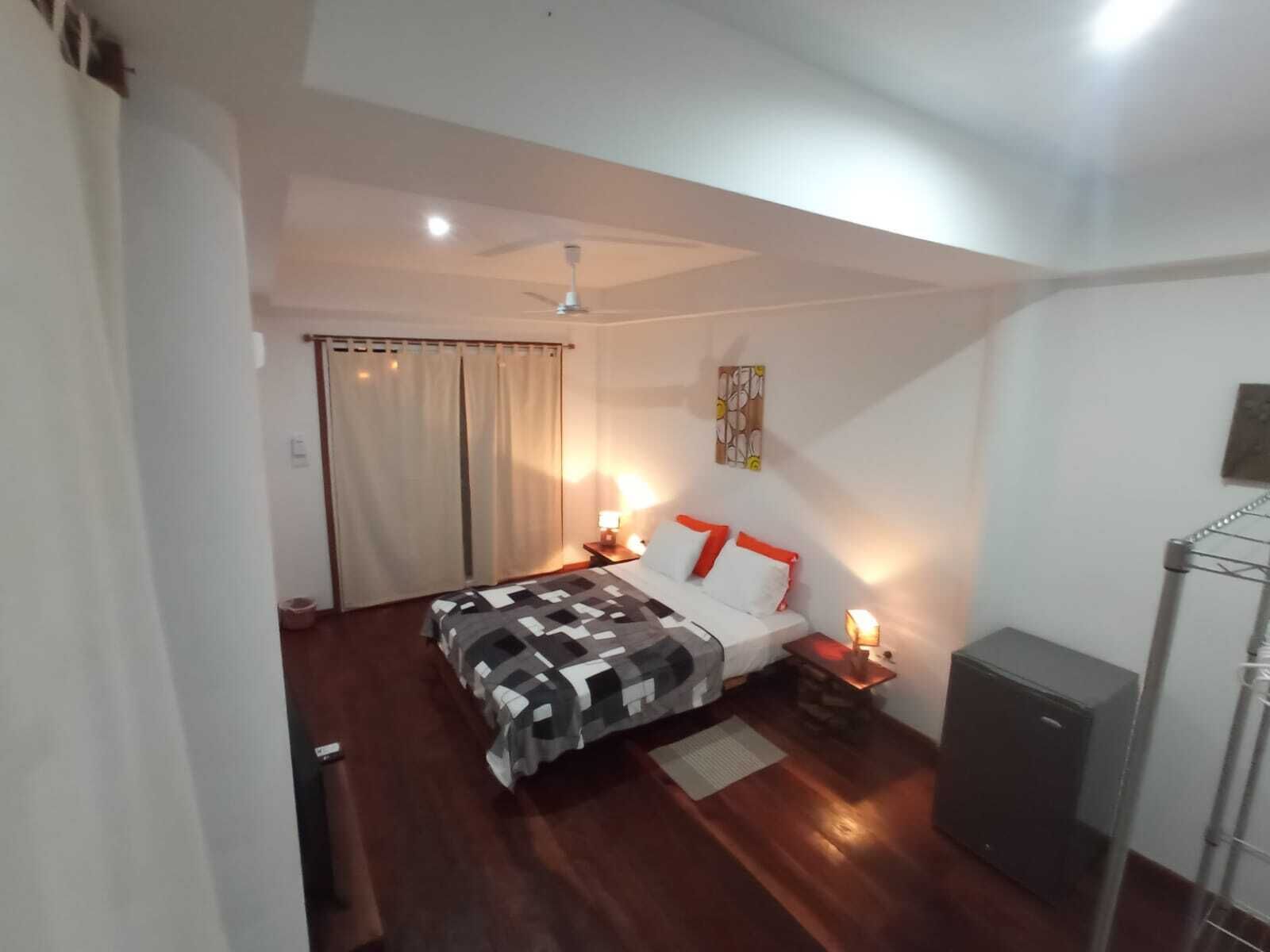 A bedroom with a bed, bedside lamps, a ceiling fan, a wardrobe, and a small desk.