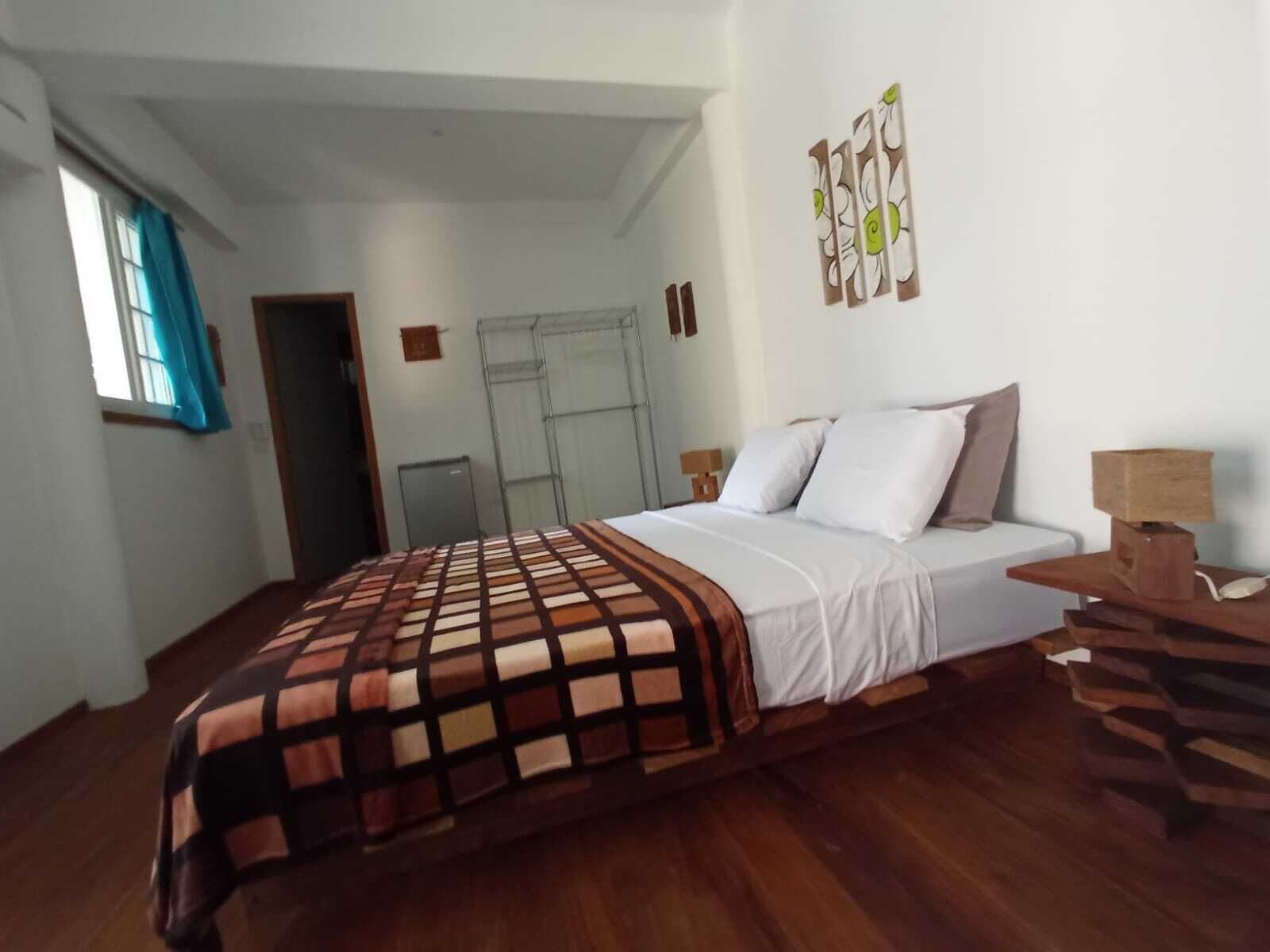 Una camera da letto con un letto, un comodino in legno, una scrivania, una finestra con tende e una porta.