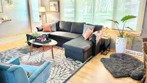 Una sala de estar moderna con un sofá modular, una mesa de centro, un sillón azul y un ventanal con vistas a zonas verdes.
