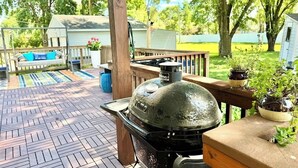 Una parrilla de barbacoa en una terraza de madera con vistas a una piscina y una casa al fondo.