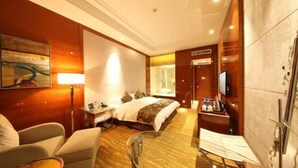 Ein Hotelzimmer mit einem Bett, einem Schreibtisch mit Lampe, einem Sessel, einem Glastisch und einem Fernseher.