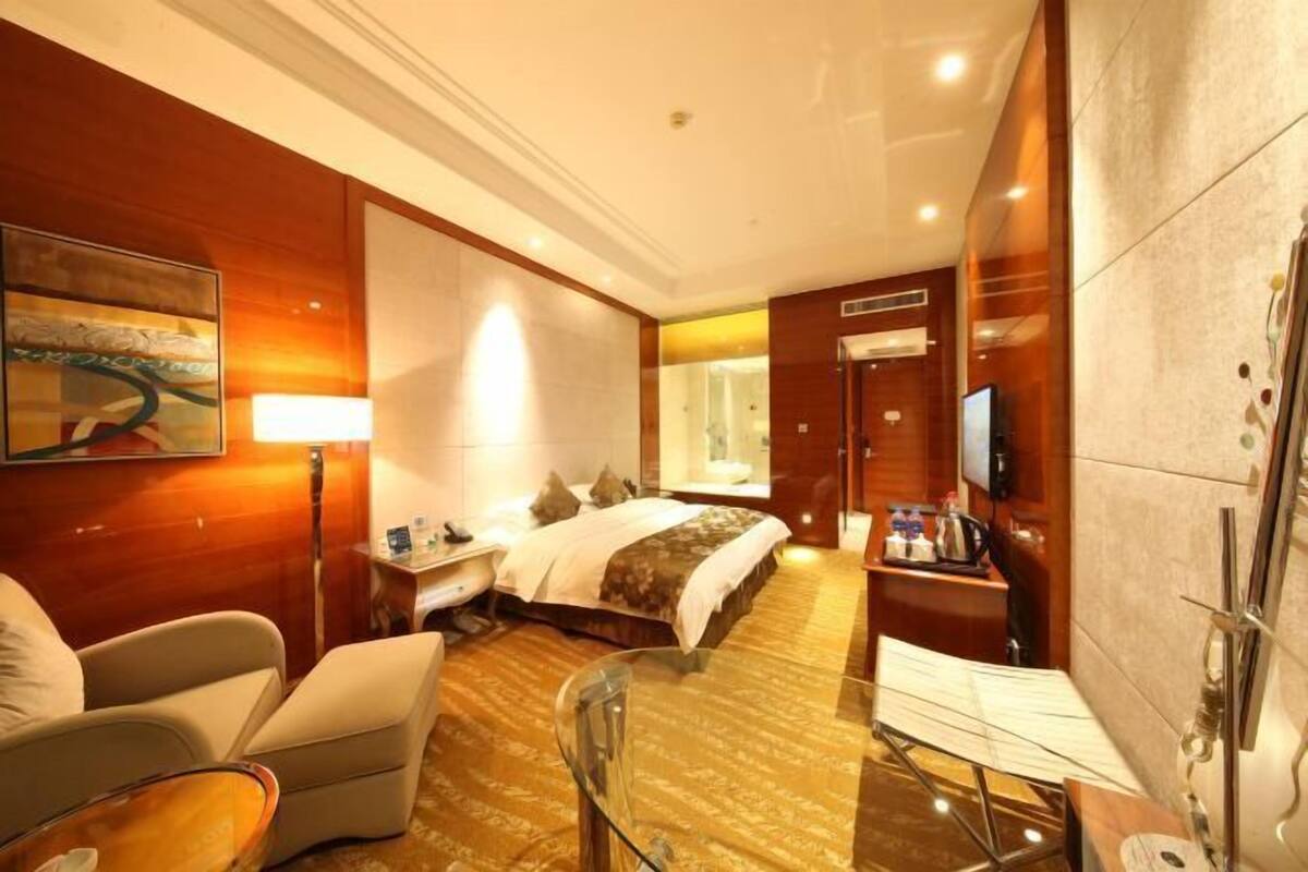 Une chambre d’hôtel avec un lit, un bureau avec une lampe, une chaise, une table en verre et un téléviseur.