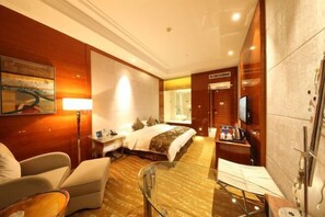 A hotel room with a bed, a desk with a lamp, a chair, a glass table, and a TV. - Wanhao Kaiyue International Hotel (Ying County)