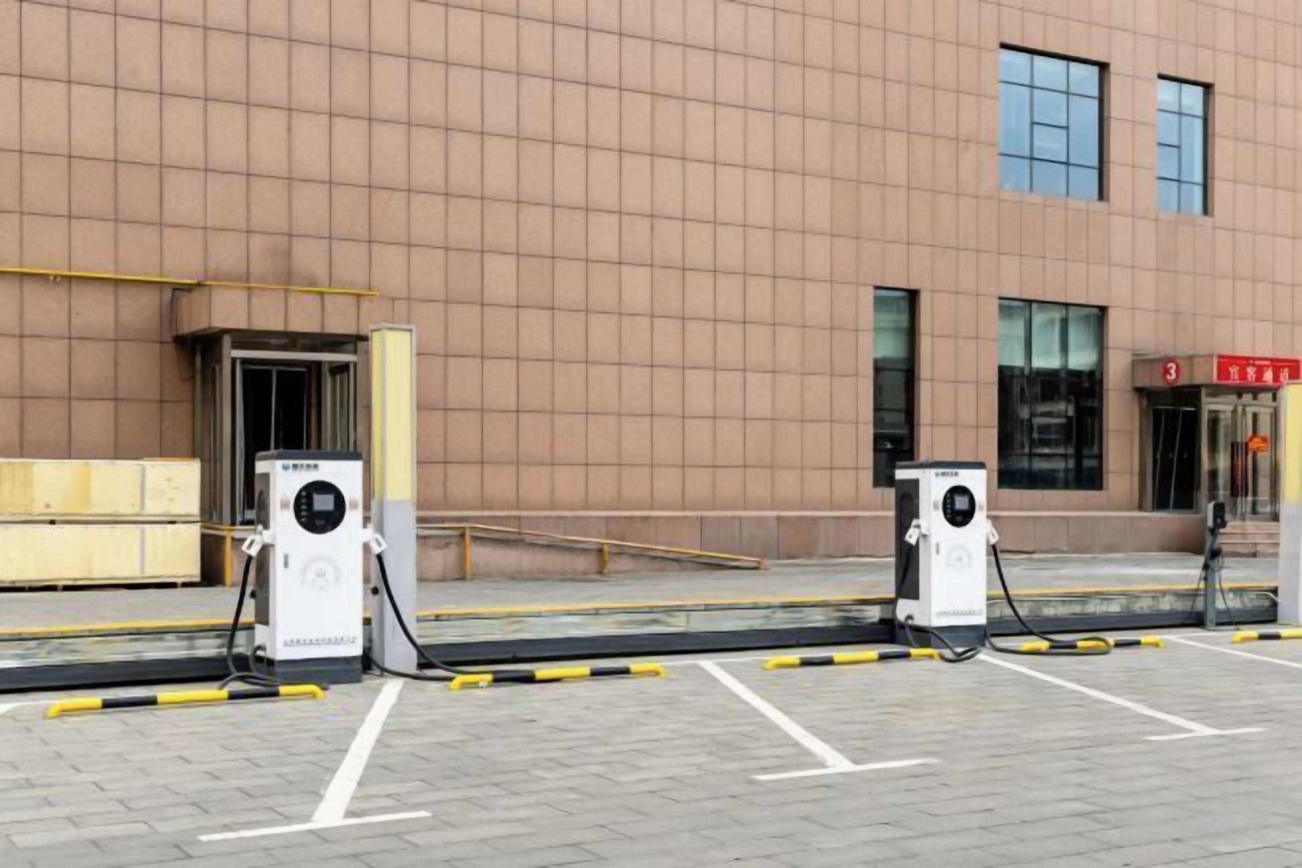 Un edificio con área de estacionamiento y dos estaciones de carga para vehículos eléctricos.