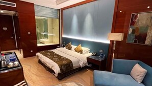 Une chambre d’hôtel avec un lit, une table de chevet, une lampe et un fauteuil bleu.