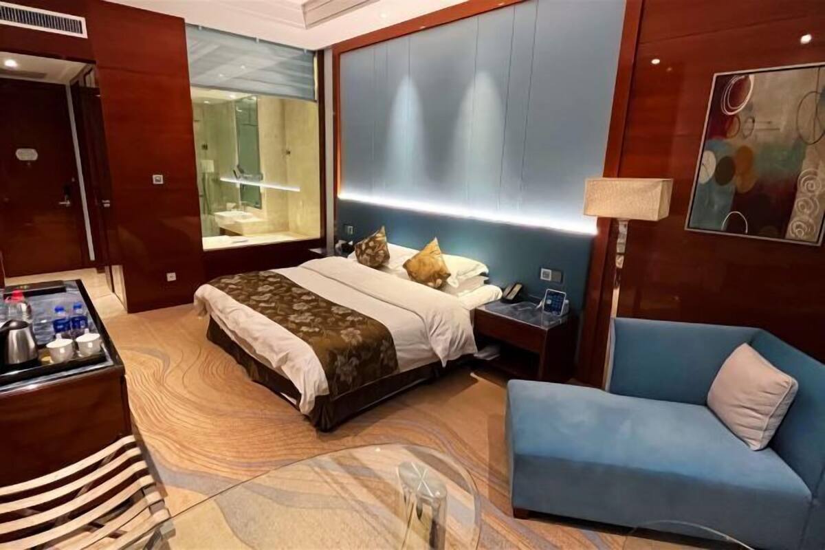 Une chambre d’hôtel avec un lit, une table de chevet, une lampe et un fauteuil bleu.