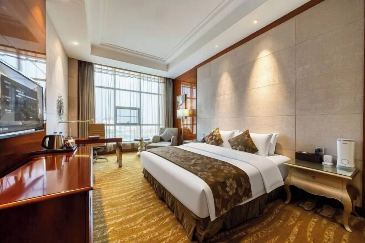 Une chambre d’hôtel avec un grand lit, un bureau, une télévision et une fenêtre avec des rideaux.