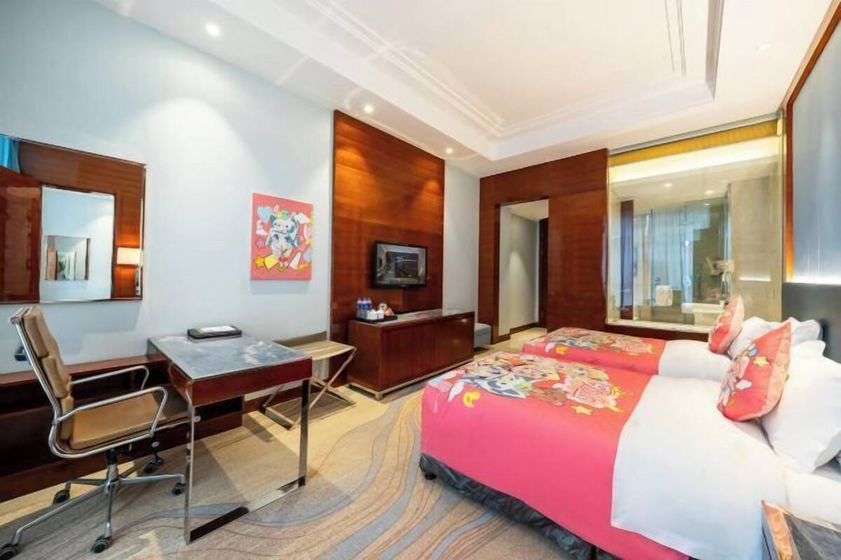 Une chambre d’hôtel équipée d’un lit, d’un bureau, d’une chaise, d’une télévision et d’un grand miroir.