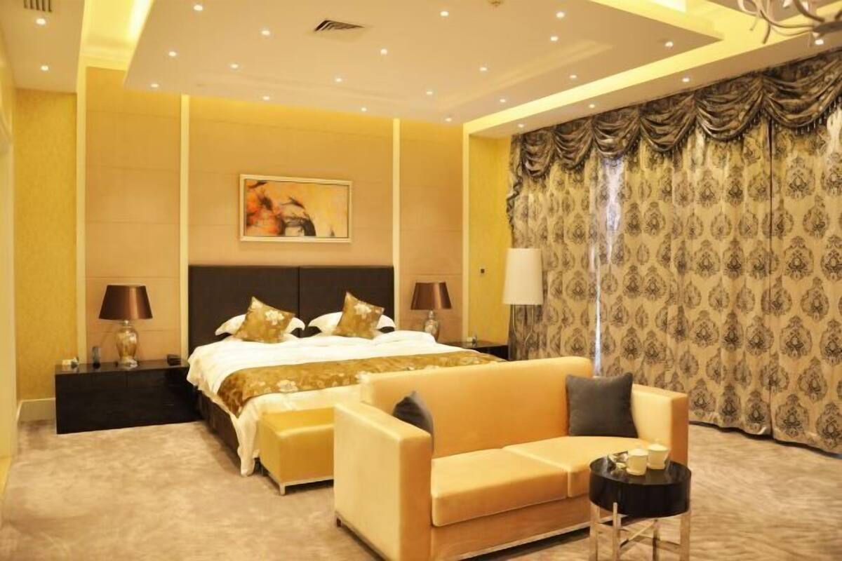 Une chambre d’hôtel comprenant un lit, deux tables de chevet, un canapé, une petite table et un rideau à motifs.