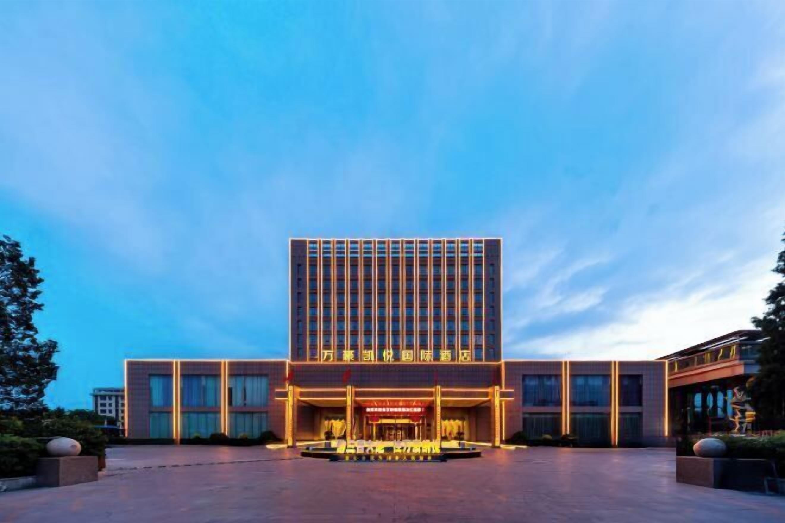 Un hotel moderno con entrada central, amplia zona de estacionamiento y fachada bien iluminada.