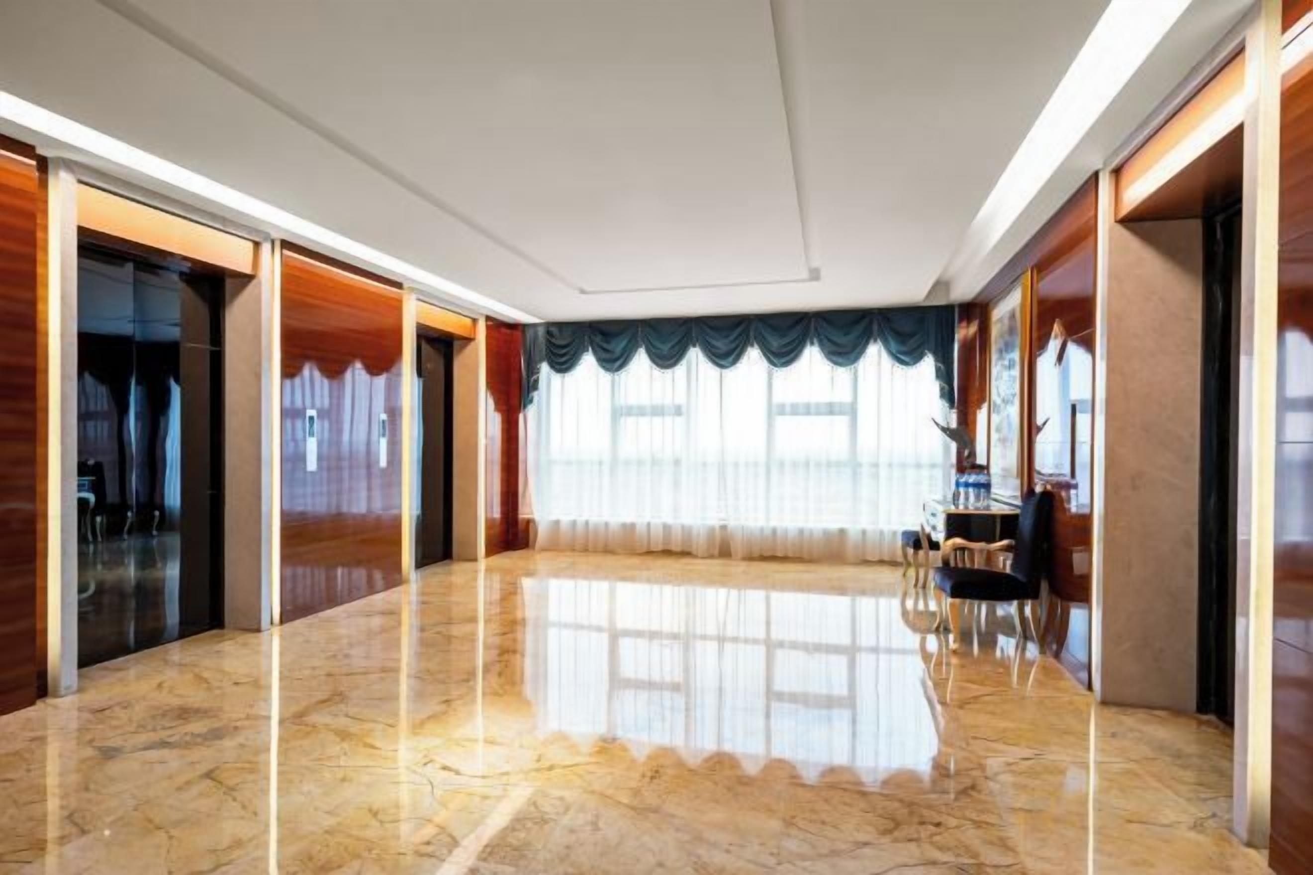 A spacious room with a polished marble floor, a large window with curtains, and a seating area with a table and chairs.