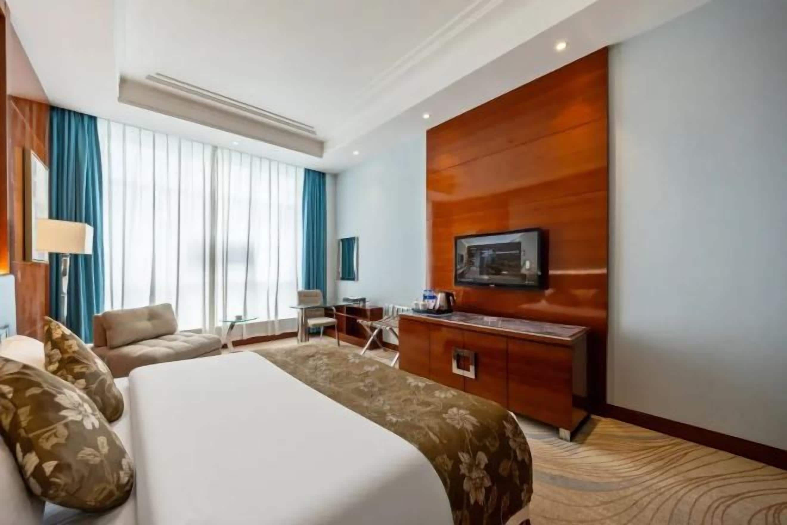 A hotel room with a large bed, a desk, a television, and a view of the city.