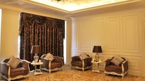 Une chambre luxueuse, meublée avec goût, dotée d’un lustre et d’une grande fenêtre agrémentée de rideaux.