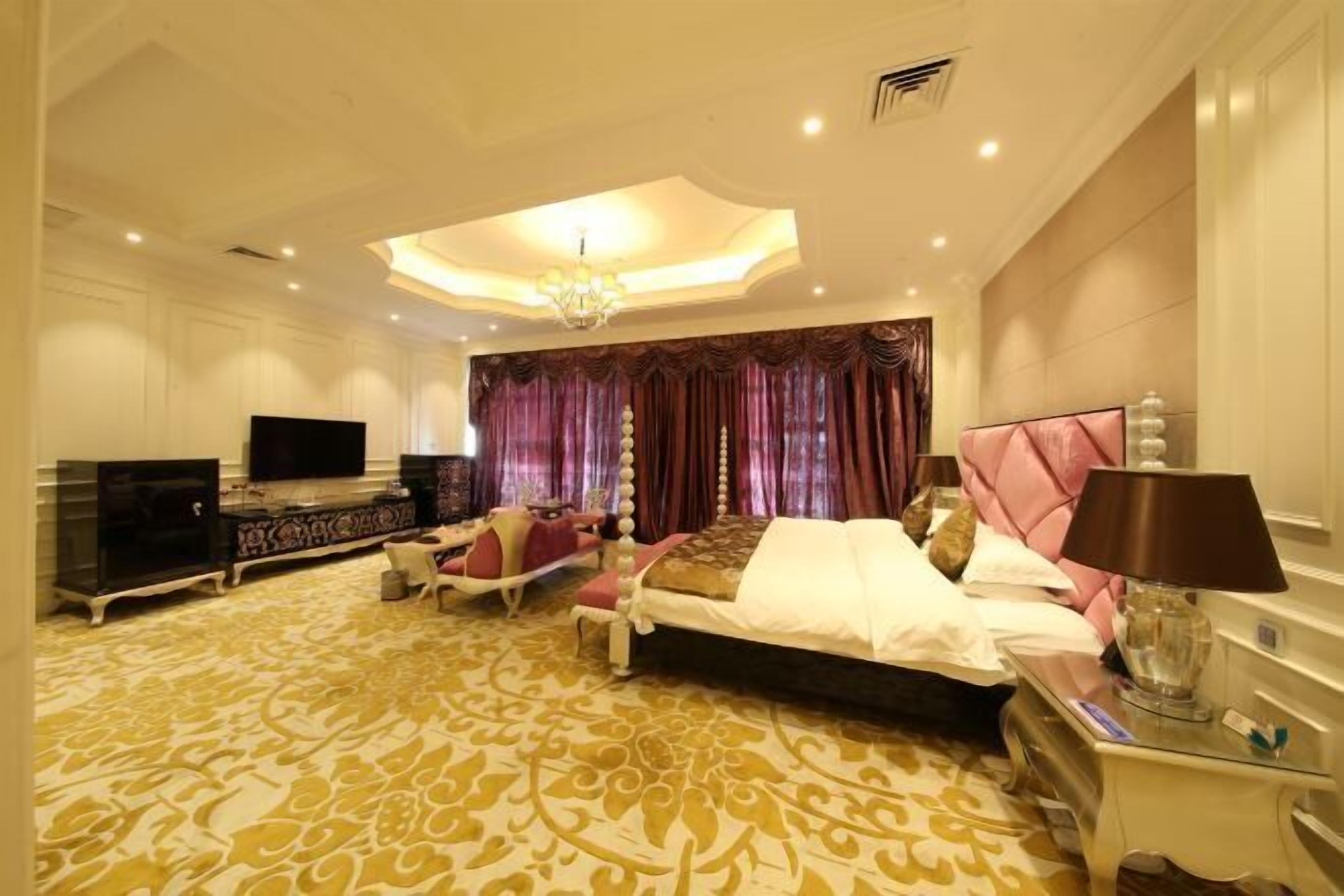 Una habitación de hotel amplia con una cama grande, televisión, escritorio y candelabro.