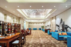 Un vestíbulo de hotel con una larga recepción, zona de estar con sofás y una gran estantería.