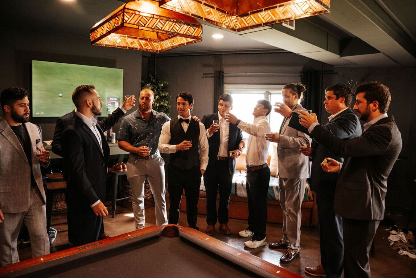 A group of men in a room with a pool table, a projector screen, and a large window.