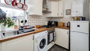 A modern kitchen with white cabinets, a stainless steel sink, a built-in washing machine, a stove, and a refrigerator.