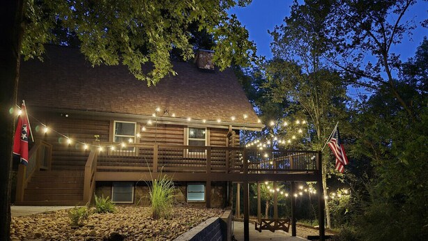 A wooden cabin with a deck, string lights, and an American flag. - Cozy log cabin, 25 mins to Broadway (Ashland City)