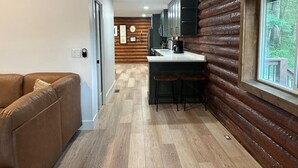A compact kitchen with a wooden accent wall, a built-in bar area, and a view through a window. - Cozy log cabin, 25 mins to Broadway (Ashland City)